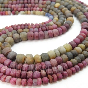 May include: A strand of multi-coloured gemstone beads. The beads are round and have a rough, textured surface. The colours of the beads are shades of pink, red, brown, and grey.