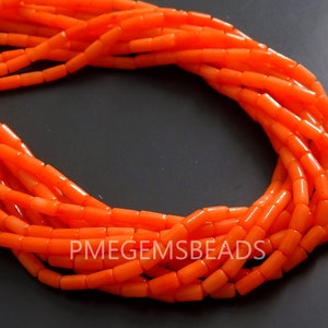 May include: A strand of bright orange cylindrical beads arranged in a circular loop. The beads have a smooth, uniform texture and are strung together on a thin cord. The text PMEGEMSBEADS is printed in white capital letters across the lower section.
