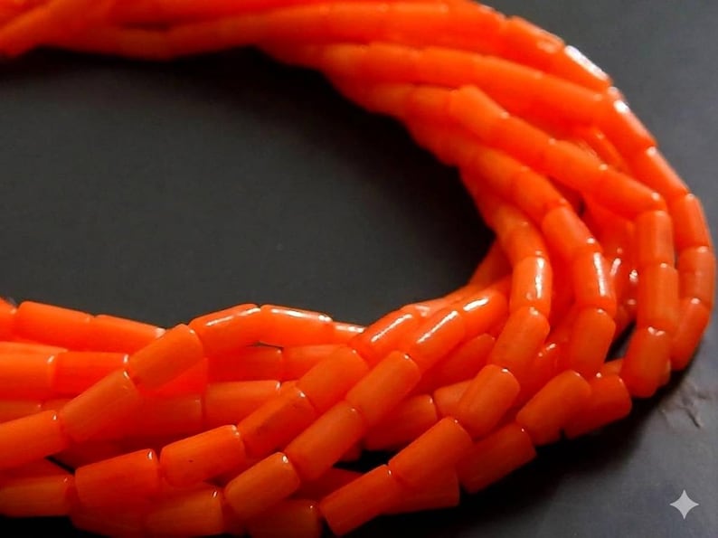 May include: A multi-strand necklace composed of numerous small, cylindrical, bright orange beads. The beads are arranged in a dense, layered formation, creating a continuous, curved loop of vibrant, uniform color throughout the entire piece.