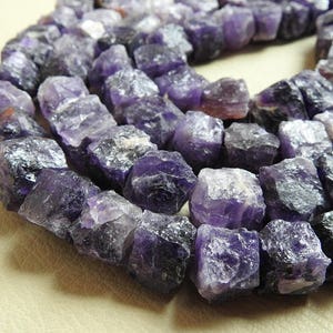 May include: A strand of purple amethyst gemstone beads, each bead is a rough, irregular cube shape.