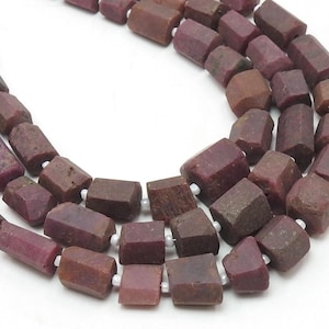 May include: A strand of dark red ruby beads with a faceted, rectangular shape. The beads are strung on a white cord.