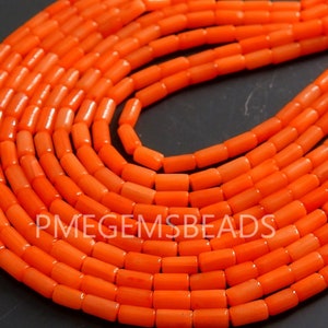 May include: A collection of bright orange cylindrical beads arranged in multiple curved rows. The beads have a smooth, uniform texture and are strung together. The text PMEGEMSBEADS is visible in white lettering across the center of the orange beads.