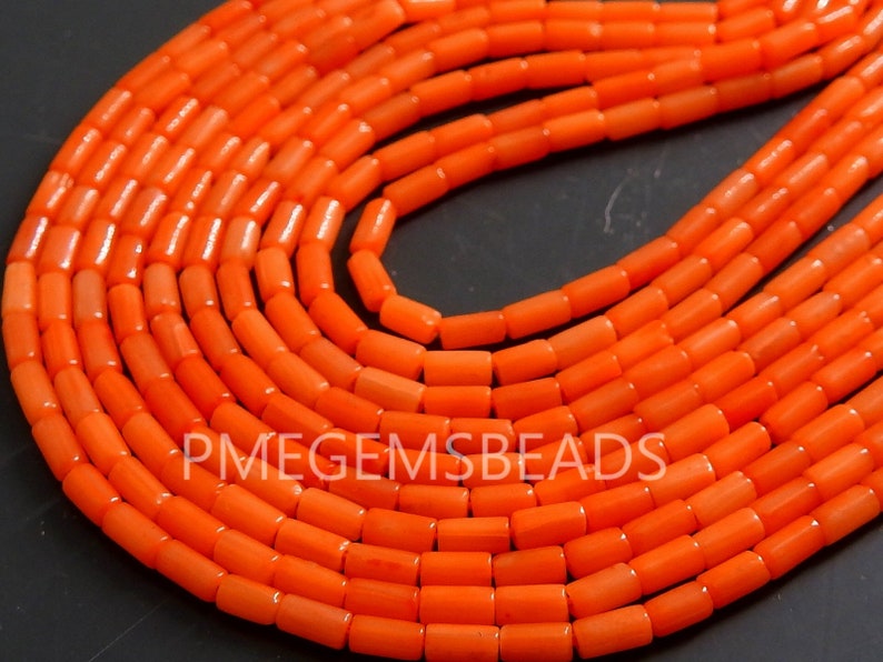 May include: A collection of bright orange cylindrical beads arranged in multiple curved rows. The beads have a smooth, uniform texture and are strung together. The text PMEGEMSBEADS is visible in white lettering across the center of the orange beads.