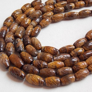 Könnte beinhalten: Eine Schnur aus braunen und goldenen Tigeraugenperlen mit einem geschnitzten Blattdesign. Die Perlen sind oval geformt und haben eine glänzende Oberfläche.