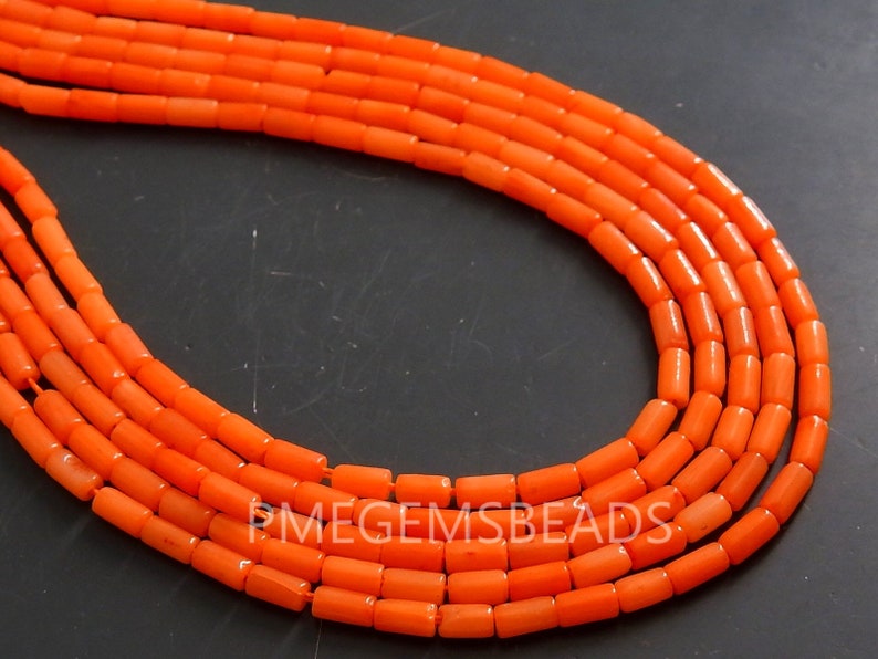 May include: Multiple strands of bright orange cylindrical beads arranged in a curved formation. The beads are uniform in shape and size, featuring a smooth, matte finish. The text PMEGEMSBEADS is visible in white lettering across the center.