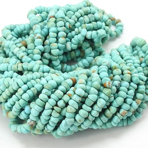 Puede incluir: Una gran colección de pequeñas cuentas redondas de color turquesa con inclusiones naturales de matriz marrón. Las cuentas están ensartadas en un cordón azul claro, formando un denso racimo circular de piezas de piedra con texturas variadas.