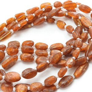 May include: A strand of brown oval-shaped beads with a metallic sheen. The beads are strung on a white thread.
