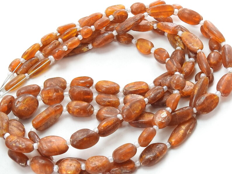 May include: A strand of brown oval-shaped beads with a metallic sheen. The beads are strung on a white thread.