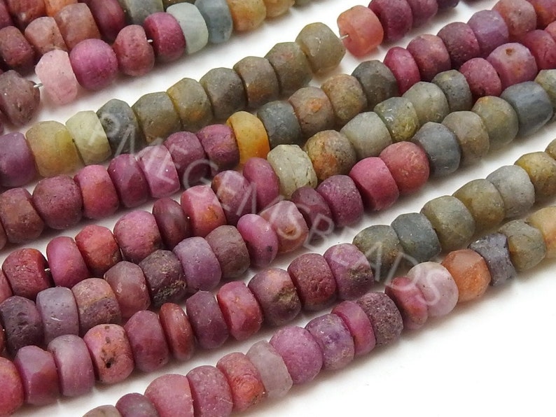 May include: A strand of multi-coloured gemstone beads. The beads are round and have a rough, textured surface. The colours of the beads include pink, red, orange, yellow, green, blue, and purple.