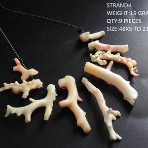 Op de afbeelding: Een ketting met negen stukken koraal in verschillende vormen en maten, geregen op een dun zwart koord. Het koraal is voornamelijk gebroken wit met roze accenten en meet tussen 48x5 en 21x7 mm. De tekst in de afbeelding luidt: STRAND-I WEIGHT:19 GRAMS QTY:9 PIECES SIZE:48X5 TO 21X7 MM.