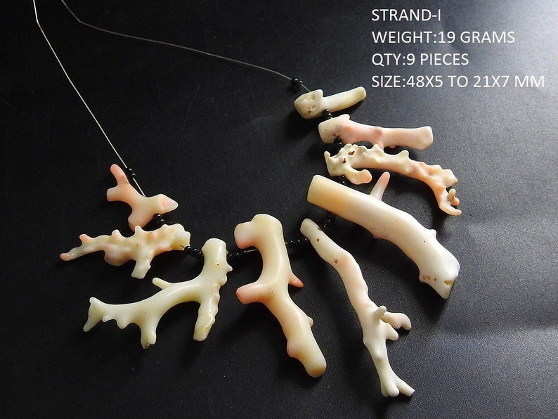 Op de afbeelding: Een ketting met negen stukken koraal in verschillende vormen en maten, geregen op een dun zwart koord. Het koraal is voornamelijk gebroken wit met roze accenten en meet tussen 48x5 en 21x7 mm. De tekst in de afbeelding luidt: STRAND-I WEIGHT:19 GRAMS QTY:9 PIECES SIZE:48X5 TO 21X7 MM.