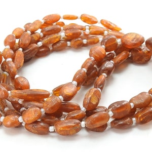 May include: A long strand of amber beads with a warm, honey-like color. The beads are oval-shaped and have a smooth, polished finish. The strand is interspersed with small, white beads.