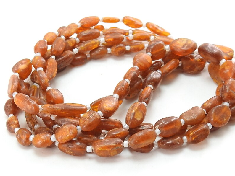 May include: A long strand of amber beads with a warm, honey-like color. The beads are oval-shaped and have a smooth, polished finish. The strand is interspersed with small, white beads.