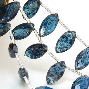 Puede incluir: Una hebra de cuentas de piedras preciosas de color azul oscuro en forma de marquesa con alambre plateado.