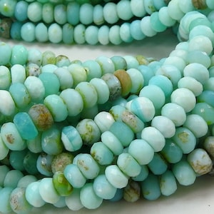 Puede incluir: Un hilo de cuentas rondelle facetadas en tonos azul claro, turquesa y verde menta. Las cuentas presentan inclusiones naturales y variaciones de color, con algunas mostrando manchas de color marrón tierra y bronceado en la superficie pulida.