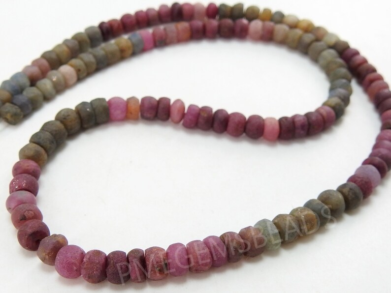May include: A strand of pink, brown and grey gemstone beads. The beads are round and have a matte finish.