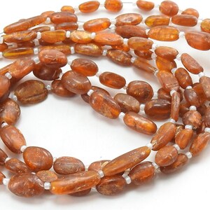 May include: A strand of oval-shaped, amber-colored beads with a slightly translucent finish. The beads are strung on a white thread.