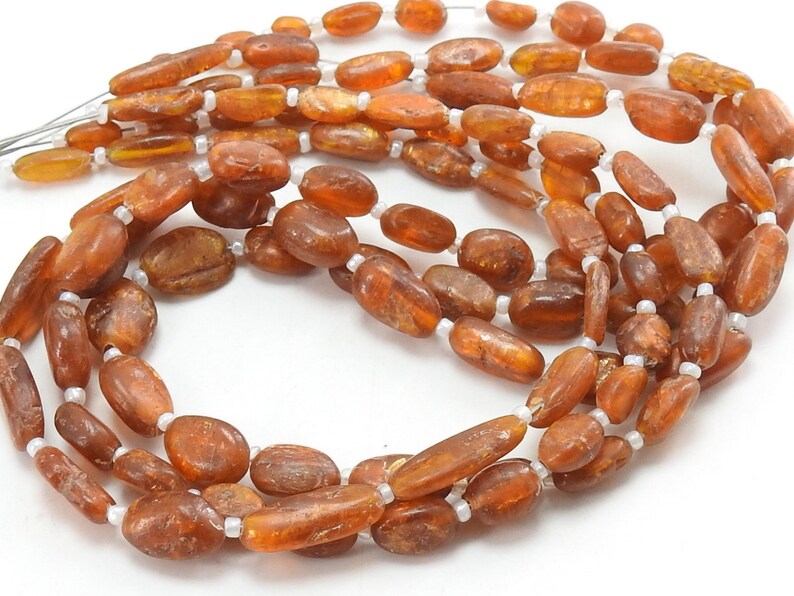 May include: A strand of oval-shaped, amber-colored beads with a slightly translucent finish. The beads are strung on a white thread.