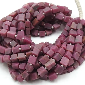 May include: A strand of deep pink, square-shaped gemstone beads. The beads are approximately 6mm in size and have a slightly irregular shape.