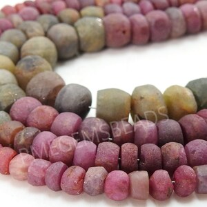 May include: A strand of faceted gemstone beads in shades of pink, brown, and green. The beads are irregular in shape and have a rough, natural finish.