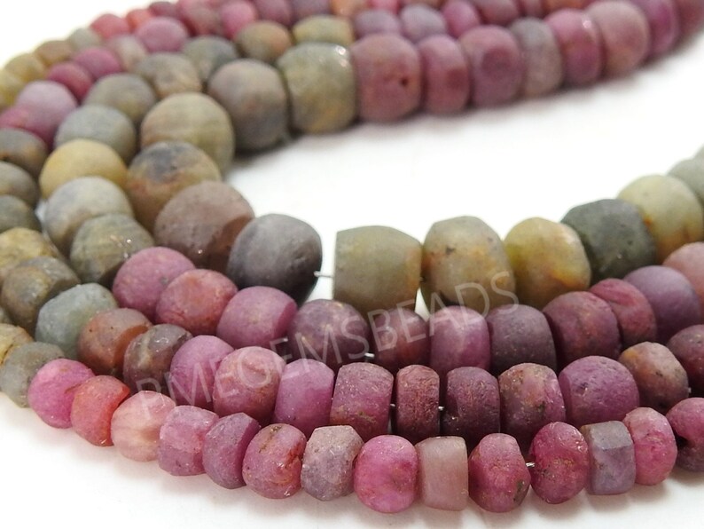 May include: A strand of faceted gemstone beads in shades of pink, brown, and green. The beads are irregular in shape and have a rough, natural finish.
