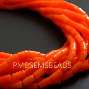 May include: A collection of vibrant orange cylindrical beads arranged in a curved formation. The beads have a smooth, polished finish and a consistent shape. The text PMEGEMSBEADS is clearly visible in white lettering across the center of the beads.