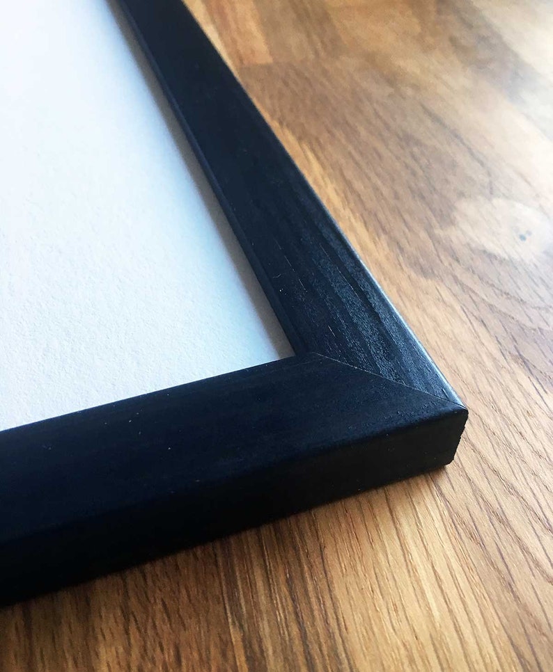 Op de afbeelding: Close-up van een zwart houten fotolijst met een gladde, matte afwerking. De lijst ligt op een houten oppervlak.