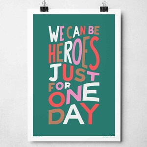 Op de afbeelding: Een tealgroene poster met de tekst "WE CAN BE HEROES JUST FOR ONE DAY" in witte, roze, rode en bruine letters.