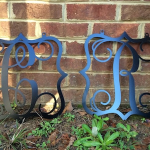 May include: Two black metal monogram signs with a decorative script font. The signs are hanging on a brick wall.