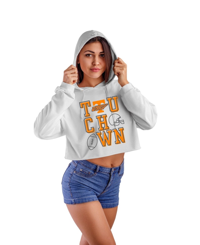 May include: White cropped hoodie with a graphic of the letters "T.U.C.H.O.W.N." in orange with a football helmet and football graphic. The letters "T.U." have a small orange graphic of the state of Tennessee.