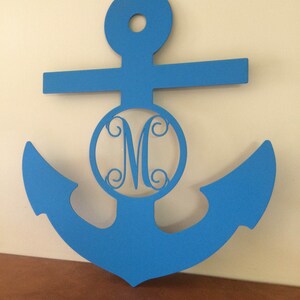 Può includere: Un'ancora di legno blu con un cerchio ritagliato al centro che presenta un monogramma bianco della lettera "M".