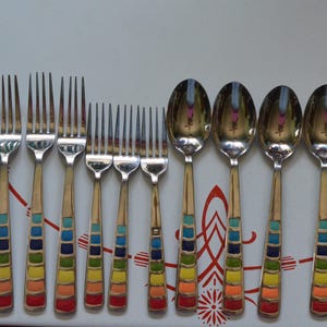 May include: A set of stainless steel flatware including forks, spoons, and a knife, each featuring a handle decorated with a vertical row of colorful enamel squares in shades of red, orange, yellow, green, blue, and purple arranged in a gradient.