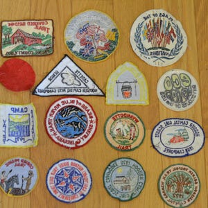 Peut inclure: Une collection de 15 patchs brod&eacute;s vintage pr&eacute;sentant divers motifs, notamment un pont couvert, un camp, une rivi&egrave;re, un drapeau et un ours. Les patchs sont principalement circulaires et rectangulaires, avec une vari&eacute;t&eacute; de couleurs et de motifs.