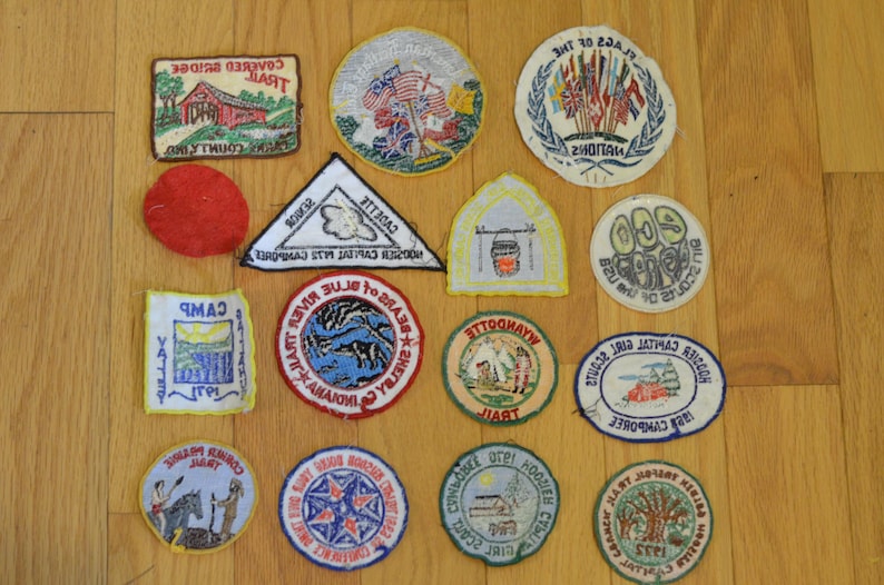 Peut inclure: Une collection de 15 patchs brod&eacute;s vintage pr&eacute;sentant divers motifs, notamment un pont couvert, un camp, une rivi&egrave;re, un drapeau et un ours. Les patchs sont principalement circulaires et rectangulaires, avec une vari&eacute;t&eacute; de couleurs et de motifs.