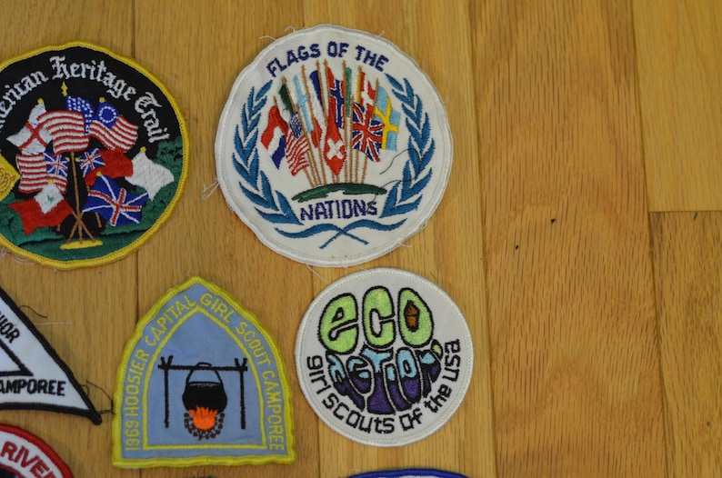 Peut inclure: Une collection de patchs brod&eacute;s color&eacute;s sur diff&eacute;rents th&egrave;mes, dont un camp de Girl Scouts, une capitale de l'Indiana et une collection de drapeaux de diff&eacute;rentes nations. Les patchs sont de forme circulaire et rectangulaire et pr&eacute;sentent une vari&eacute;t&eacute; de couleurs et de motifs.