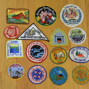 Peut inclure: Une collection de 14 patchs brod&eacute;s color&eacute;s pr&eacute;sentant divers motifs li&eacute;s aux Girl Scouts et aux Boy Scouts. Les patchs comportent des textes tels que "Covered Bridge Trail", "American Heritage Trail", "Drapeaux des Nations", "Eco Girl Scouts des &Eacute;tats-Unis", "Camp Gallahue", "Bears of Blue River Trail", "Wyandotte Trail", "Hoosier Capital Girl Scouts", "Golden Trefoil Trail", "Corner Prairie Trail", "Cadette Senior", "Hoosier Capital 1972 Camporee", et "1968 Camporee".
