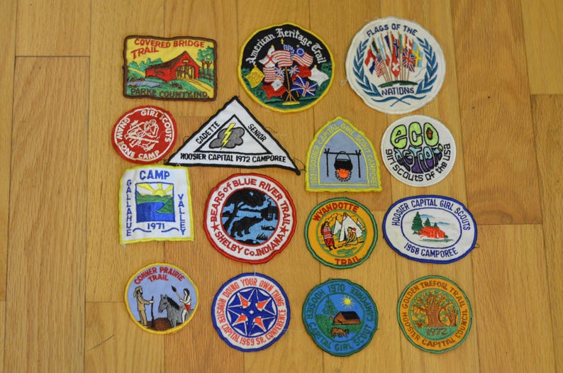 Peut inclure: Une collection de 14 patchs brod&eacute;s color&eacute;s pr&eacute;sentant divers motifs li&eacute;s aux Girl Scouts et aux Boy Scouts. Les patchs comportent des textes tels que "Covered Bridge Trail", "American Heritage Trail", "Drapeaux des Nations", "Eco Girl Scouts des &Eacute;tats-Unis", "Camp Gallahue", "Bears of Blue River Trail", "Wyandotte Trail", "Hoosier Capital Girl Scouts", "Golden Trefoil Trail", "Corner Prairie Trail", "Cadette Senior", "Hoosier Capital 1972 Camporee", et "1968 Camporee".