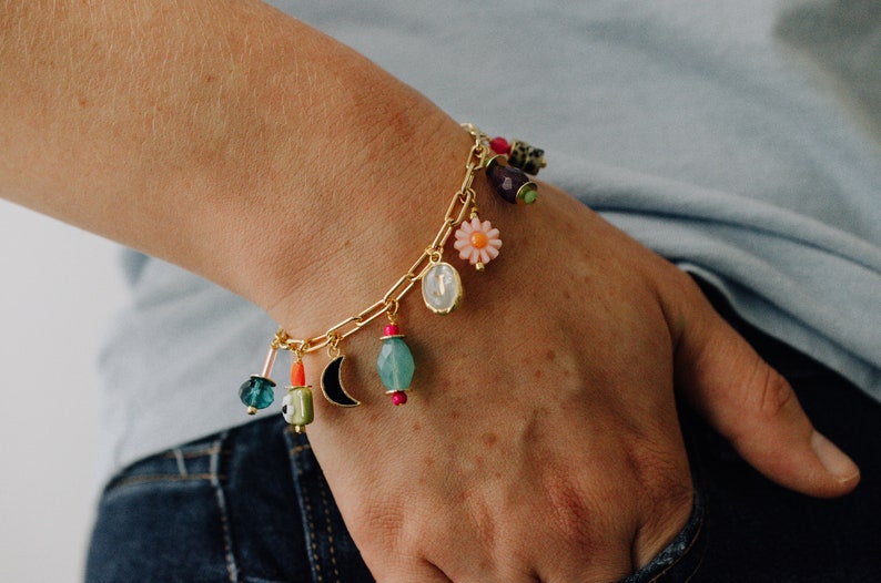 May include: A gold charm bracelet with a variety of colorful charms, including a flower, a crescent moon, a green bead, and a blue bead.
