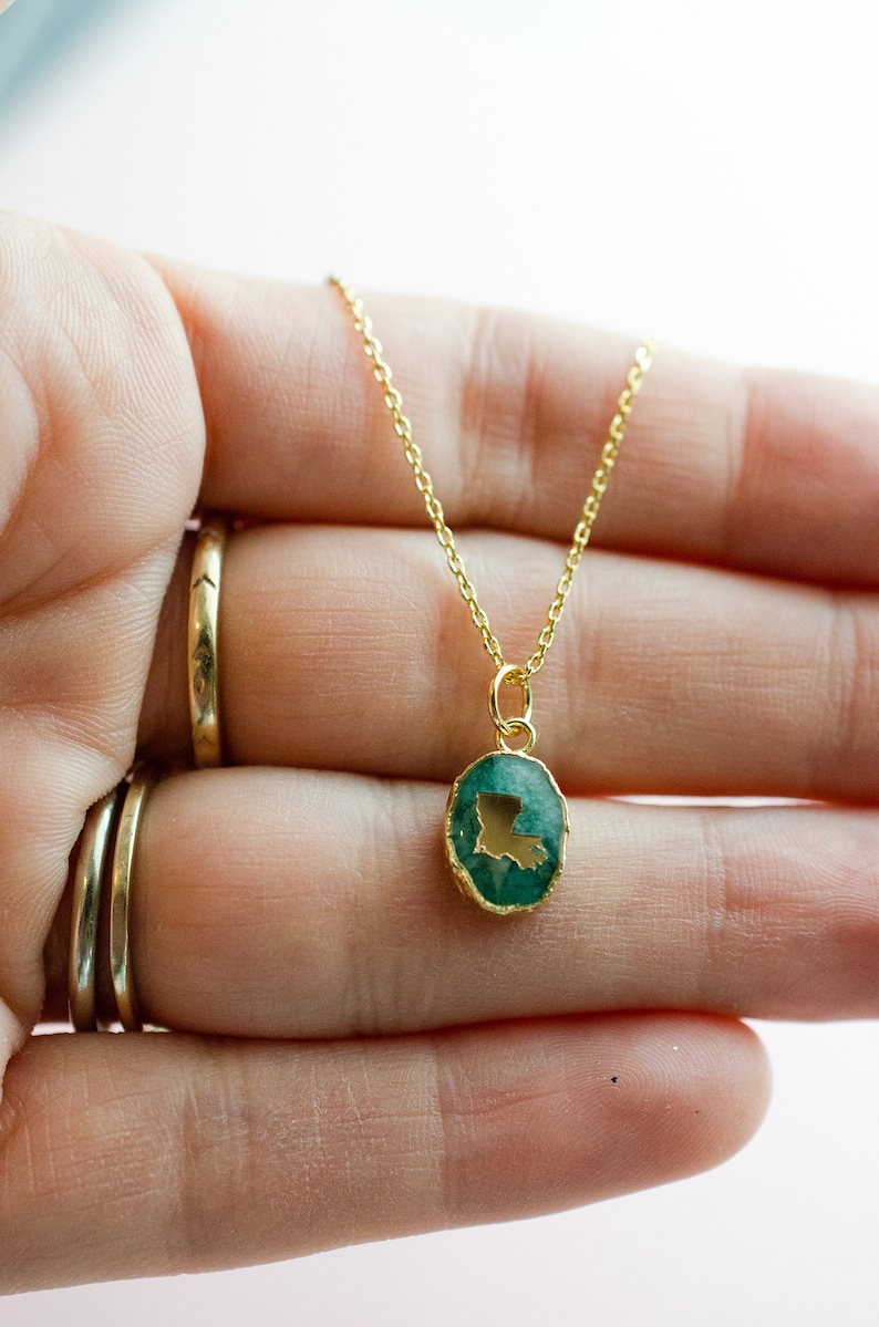 May include: A gold chain necklace with a green oval pendant featuring the outline of the state of Louisiana.