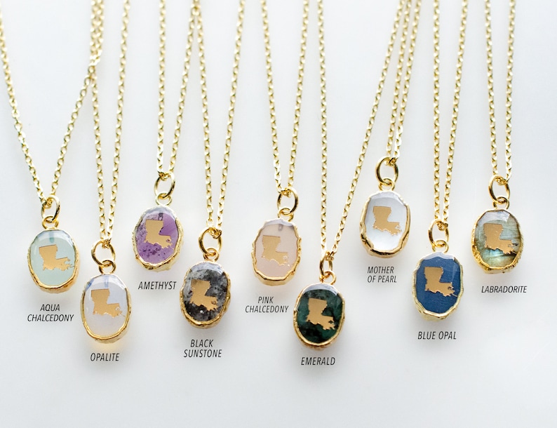 May include: Ten gold necklaces with pendants featuring the outline of the state of Louisiana. Each pendant is made of a different gemstone, including amethyst, aqua chalcedony, black sunstone, blue opal, emerald, labradorite, mother of pearl, opalite, and pink chalcedony.