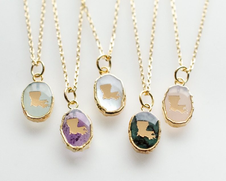 May include: Five gold necklaces with pendants featuring the state of Louisiana in gold on different colored stones. The stones are green, purple, white, pink, and light green.