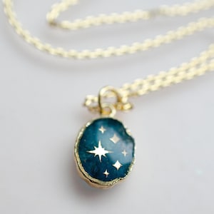 Op de afbeelding: Een gouden ketting met een blauwe en gouden hanger met een stervormig ontwerp.