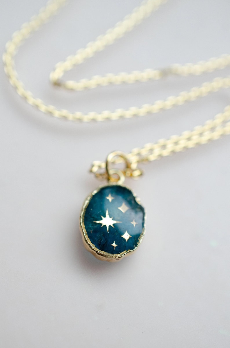 Op de afbeelding: Een gouden ketting met een blauwe en gouden hanger met een stervormig ontwerp.