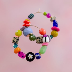 May include: A pair of colourful hoop earrings featuring a variety of beads, including green, blue, pink, orange, yellow and black. The beads are arranged in a random pattern and some have a polka dot design.