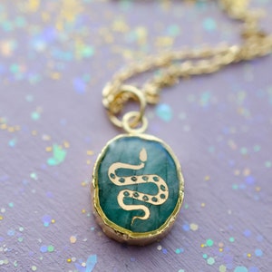 May include: A gold chain necklace with a green oval pendant featuring a gold snake design.