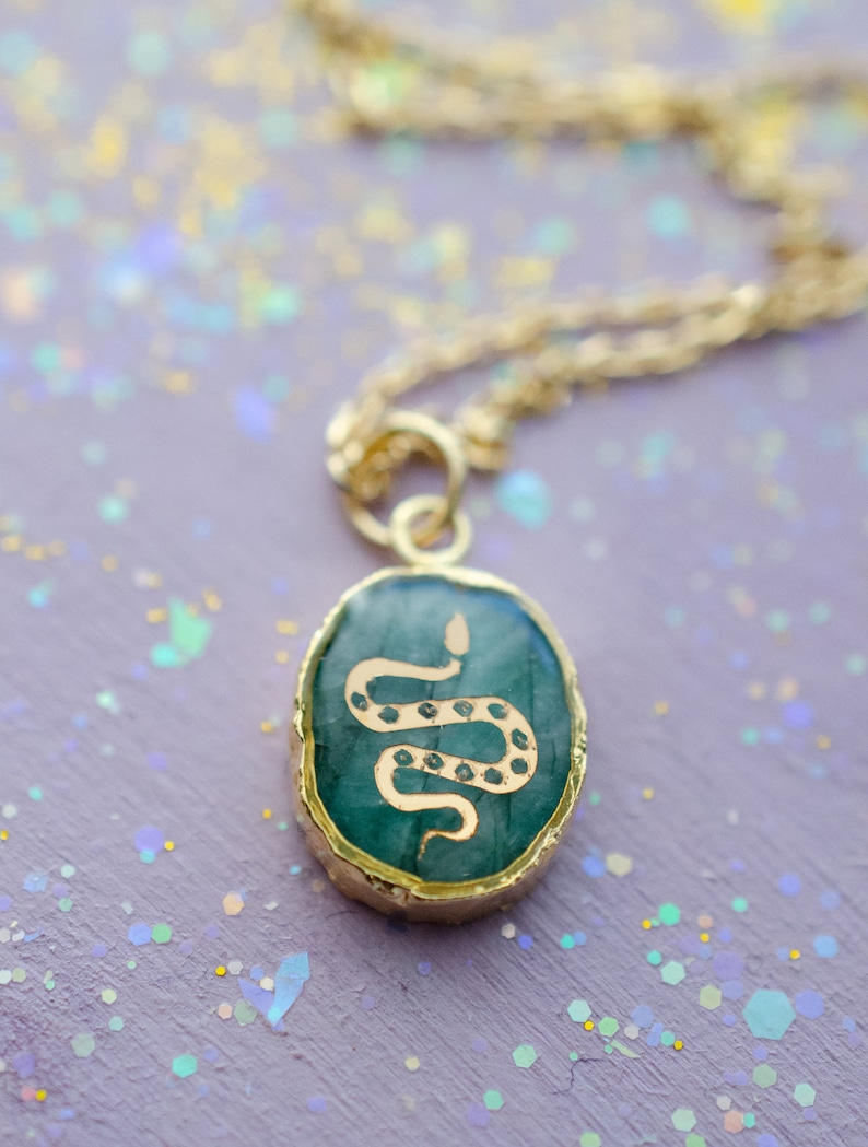 May include: A gold chain necklace with a green oval pendant featuring a gold snake design.
