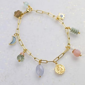 May include: Gold chain bracelet with multiple charms, including a crescent moon, a star, a cloud, a Libra zodiac sign, and various colored stones.