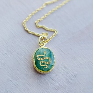May include: A gold chain necklace with a green oval pendant featuring a gold snake design.
