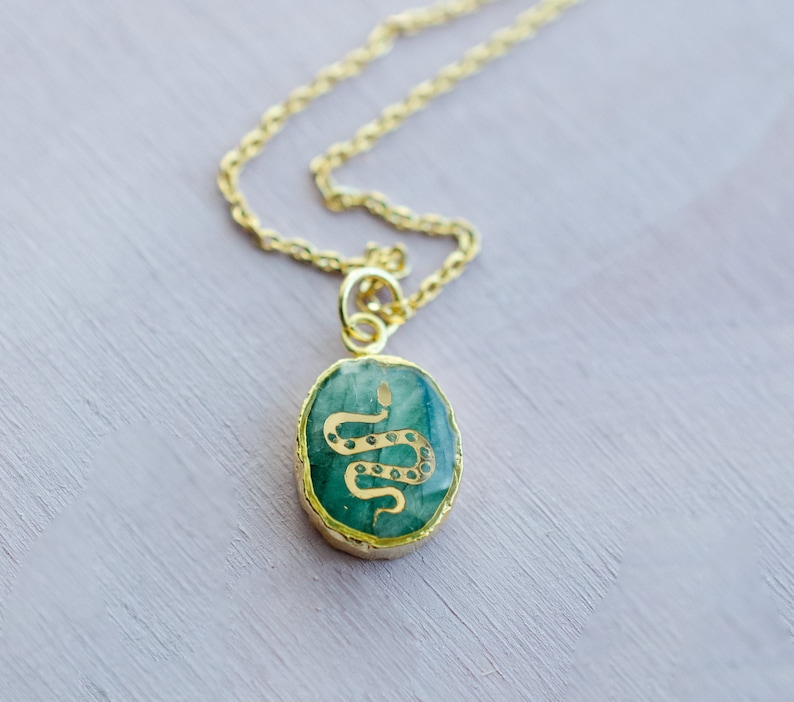 May include: A gold chain necklace with a green oval pendant featuring a gold snake design.