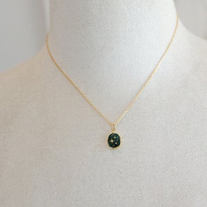 Op de afbeelding: Een gouden ketting met een donkergroene ovale hanger met een ontwerp van gouden sterren.